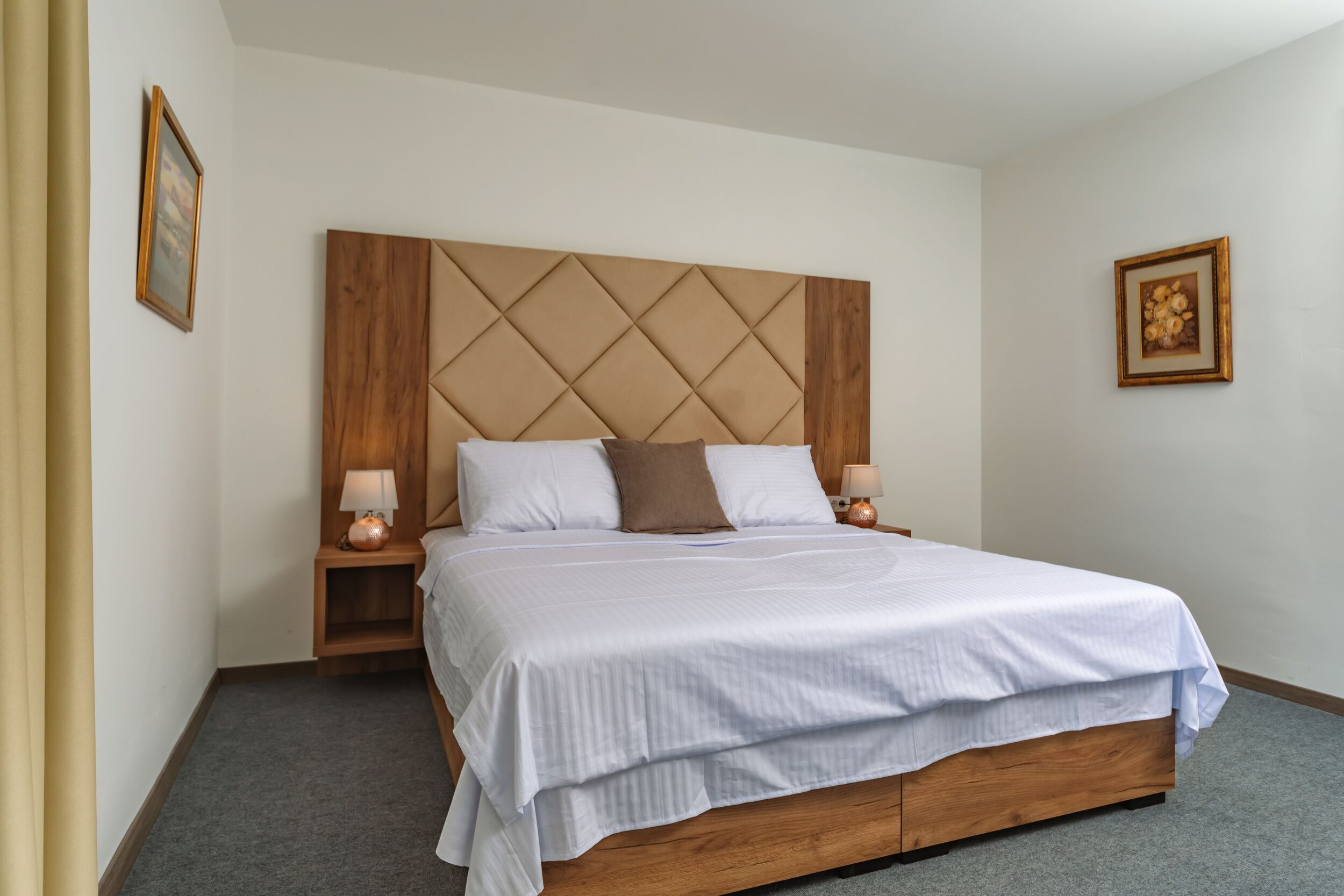 Una cama bien hecha con un cabecero de madera, dos mesitas de noche con lámparas y un cuadro en la pared.