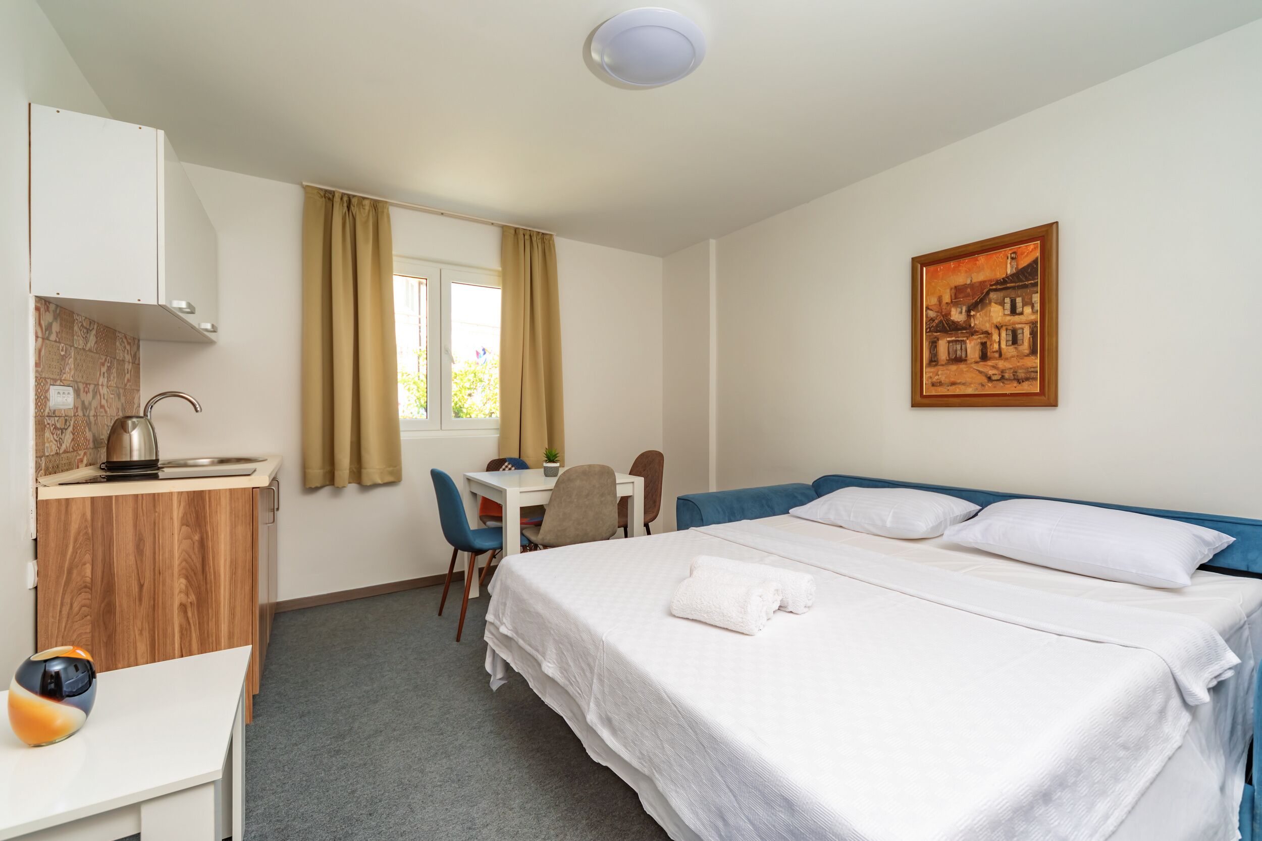 Una camera d'albergo con un letto, una scrivania, una sedia, un tavolino e un quadro appeso al muro.
