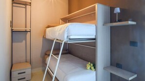 Un lit superposé avec une échelle, une petite table de chevet et une étagère avec une lampe.