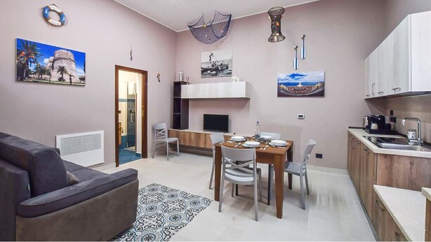 Un salon avec un canapé, une table à manger avec des chaises, un coin cuisine avec des placards et un évier, et un téléviseur posé sur un meuble.