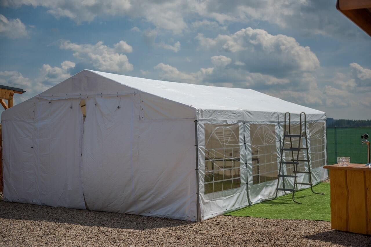 Una grande tenda bianca con una scala e un piccolo tavolo di legno con un bicchiere.