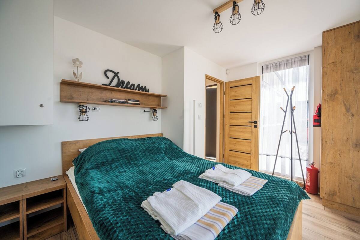 Un dormitorio con una cama, un estante de madera con el letrero 'Dream', una escalera y una ventana con cortinas de gasa.