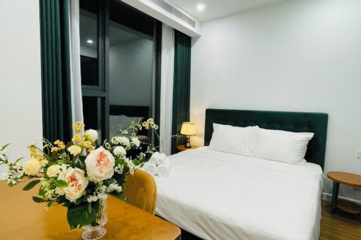 Una habitación de hotel con una cama, una mesa con un florero y una ventana con cortinas.
