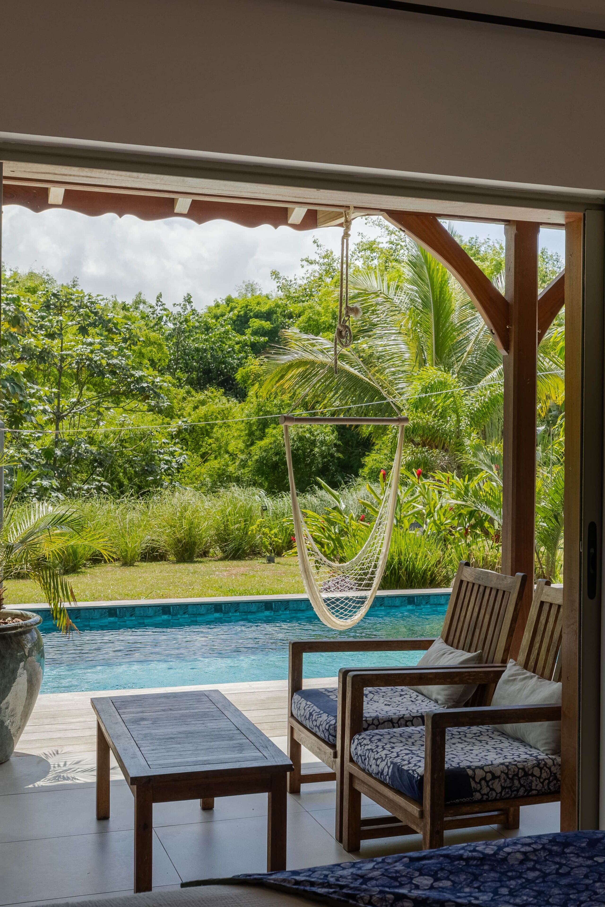 Uma área à beira da piscina com uma rede, cadeiras de madeira e uma mesa.