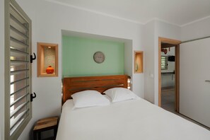 Quarto com cabeceira de madeira, cama com roupa de cama branca, mesa de cabeceira pequena e uma parede verde.