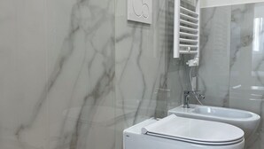 A bathroom with a toilet, bidet, and a towel warmer mounted on the wall. - The New Guesthouse Vatican (Rome)
