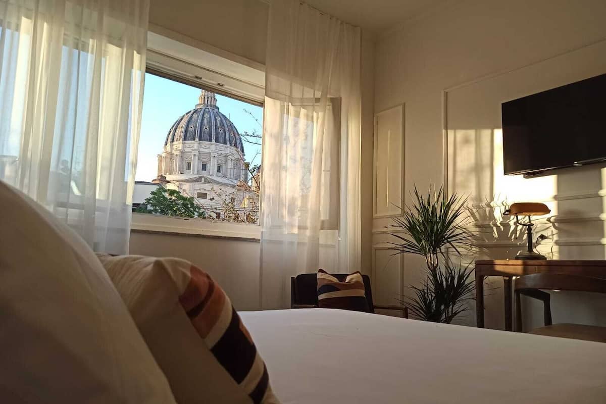 Une chambre d’hôtel avec un lit, un bureau doté d’une lampe, une télévision et une vue sur un grand immeuble par la fenêtre.