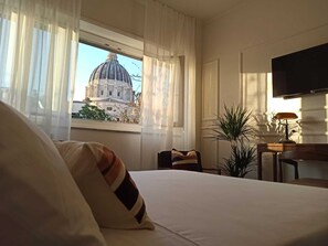 Une chambre d’hôtel avec un lit, un bureau doté d’une lampe, une télévision et une vue sur un grand immeuble par la fenêtre.
