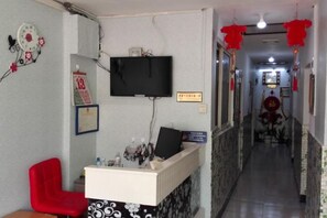 A hotel reception area with a red chair, a flat-screen TV, a clock, and a framed certificate on the wall.