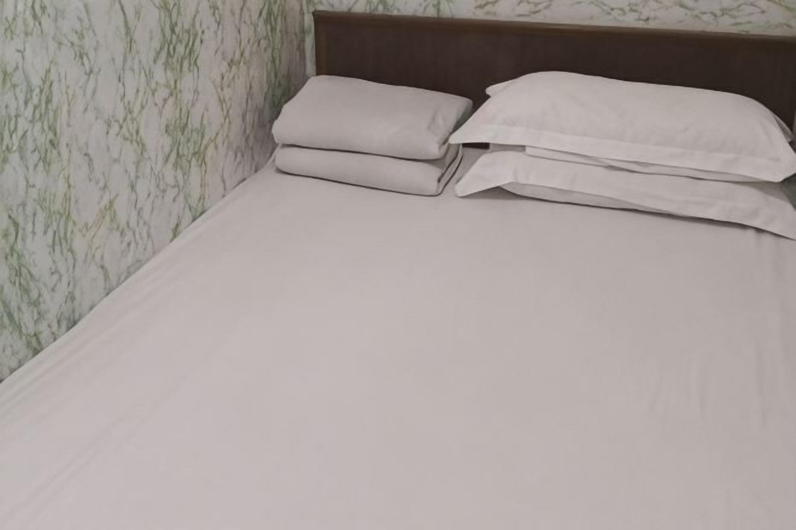 A bed with a wooden headboard, white linens, and a marble-patterned wall.