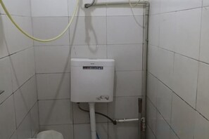 A white tiled bathroom with a white toilet, a visible pipe, and a yellow hose.