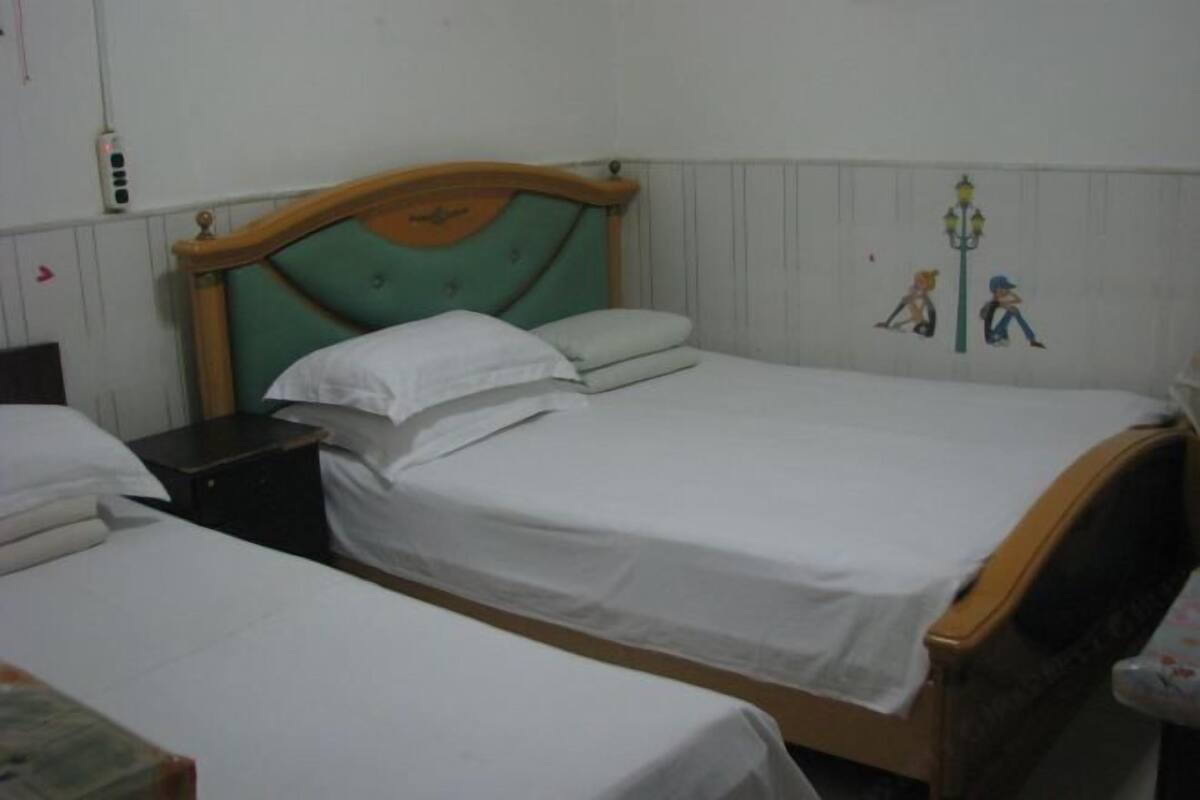 A room with two single beds, wooden headboards, white bedding, a nightstand, and a wall-mounted lamp.