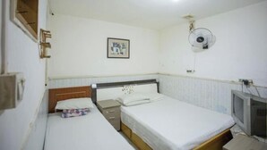 Um quarto pequeno e simples com duas camas, uma televisão e um ventilador fixado na parede.