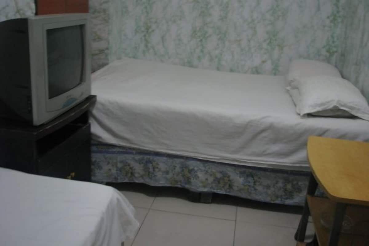 A room with a bed, a television on a stand, and a wooden chair.