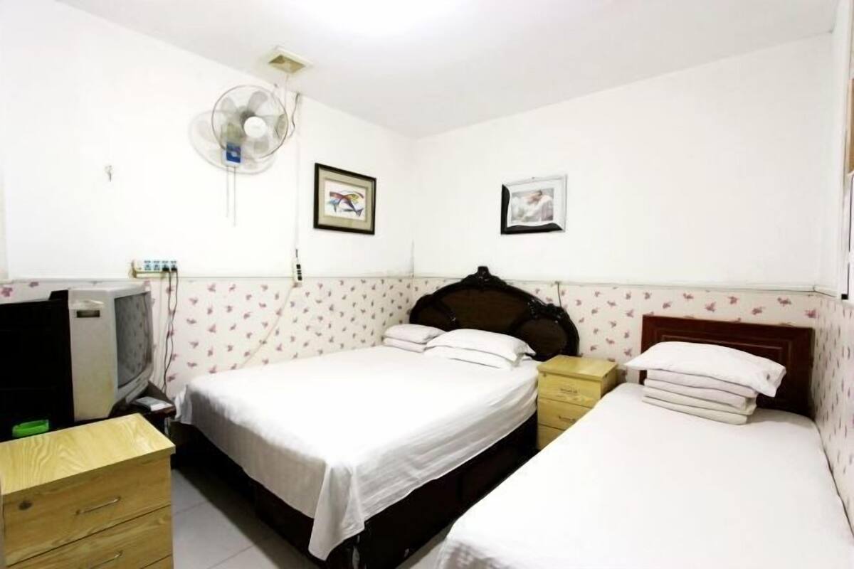 A bedroom with two beds, a desk, a chair, a fan, and a TV.