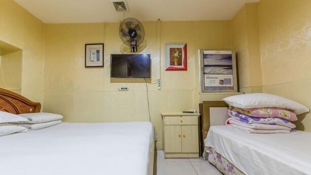 Quarto de hotel com duas camas, um pequeno armário, uma televisão e um ventilador.