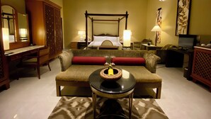 A hotel room with a four-poster bed, a sitting area with a sofa and a small table, a desk with a chair, and a large mirror. - Landmark Cenang (Langkawi)