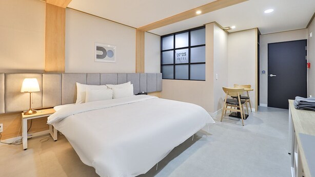 Una camera d'albergo con un letto, un comodino, una lampada, una finestra e una porta.