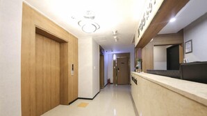 Un'area della reception di un hotel con scrivania in legno, bancone reception e un corridoio che porta a una porta.