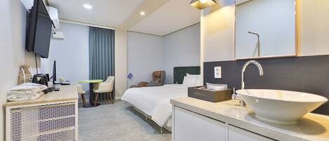 A hotel room with a bed, bedside table, desk, chair, and a large mirror.