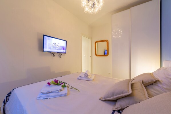 Une chambre d’hôtel avec un lit, un téléviseur fixé au mur, un miroir et un lustre.