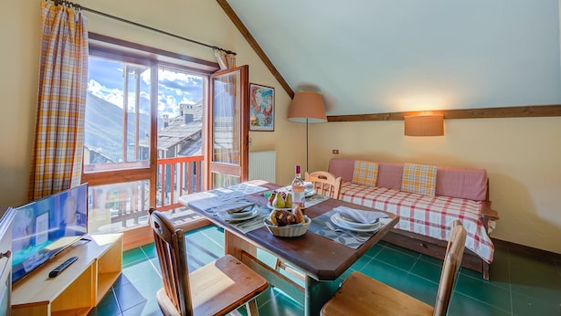 A cozy dining area with a table set for two, a television, and a view of the mountains through the window. - Grange Hike Ski - 19C Sestriere (Sauze di Cesana)