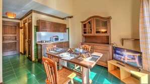 A dining area with a wooden table, chairs, and a television. There is a kitchen area with cabinets and a microwave. - Grange Hike Ski - 19C Sestriere (Sauze di Cesana)