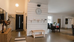 Un vaste espace de vie agrémenté d’un mur en bois, d’une horloge ronde de style ancien, d’une table à manger avec des chaises et d’un petit banc en bois.