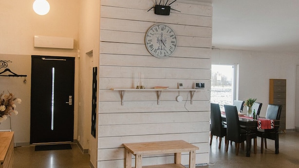 Un vaste espace de vie comprenant un banc en bois, une table à manger avec des chaises, une horloge murale et un luminaire suspendu.