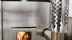 Un poêle à bois doté d’une cheminée en métal, avec un feu qui crépite à l’intérieur et une grille métallique à l’avant.