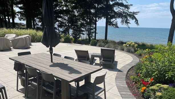 Een terras buiten met een houten tafel en stoelen, omgeven door een tuin vol kleurrijke bloemen.