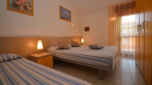 A hotel room with two beds, a nightstand, a lamp, and a window with curtains. - Selene C1-7 in Bibione (San Michele al Tagliamento)