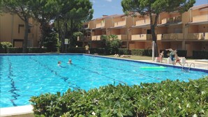 A swimming pool surrounded by apartment buildings with balconies, trees, and a clear sky. - Selene C1-7 in Bibione (San Michele al Tagliamento)