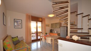 A cozy living room with a sofa, a dining table with chairs, a kitchen area with a microwave, and a staircase. - Selene C1-7 in Bibione (San Michele al Tagliamento)