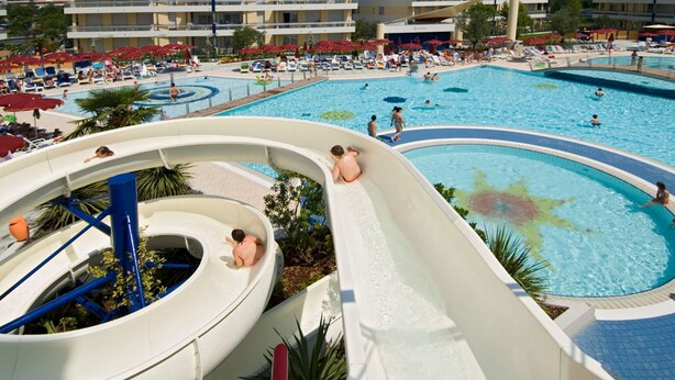 Ein großer Außenpool mit mehreren Wasserrutschen, umgeben von Liegestühlen und Sonnenschirmen.