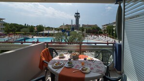 Ein Balkon mit Frühstückstisch, mit Blick auf einen Swimmingpool und einen Turm.