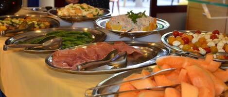 A buffet table with various food items including meats, vegetables, and fruits.
