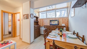 A cozy kitchen with wooden cabinets, a dining table set for four, and a large window above the sink. - La Tana Dell Ermellino 3 Ski In Ski Out (Sestriere)