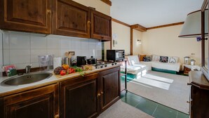 A kitchen with wooden cabinets, a sink, and a countertop with various items. There is a dining area with a table and chairs, and a bed in the background. - Grange Hike Ski - Grange Terrace Suite (Sauze di Cesana)