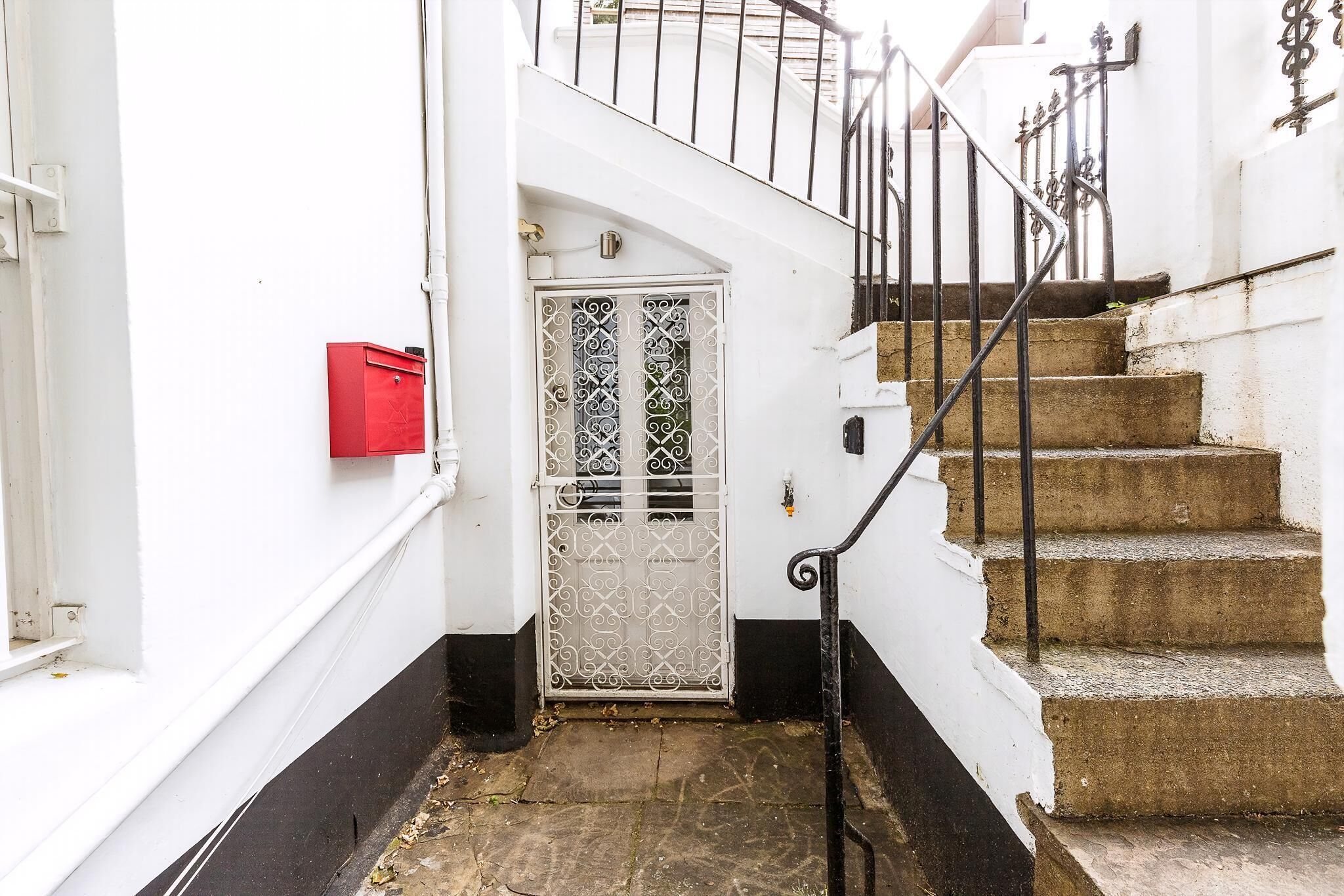 A white exterior with a metal gate, a red mailbox, and a staircase with black railings.