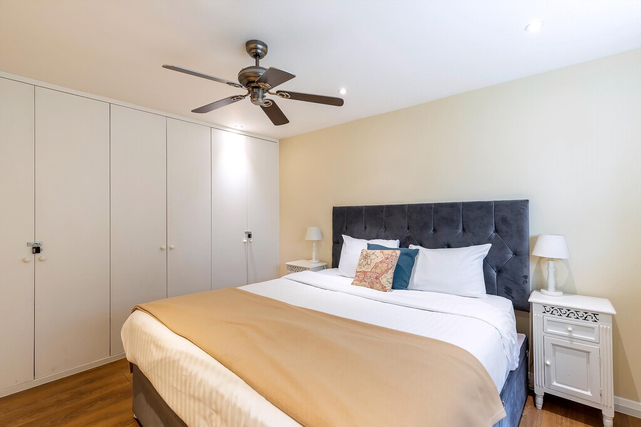 A bedroom with a bed, a ceiling fan, a nightstand, and a wardrobe.