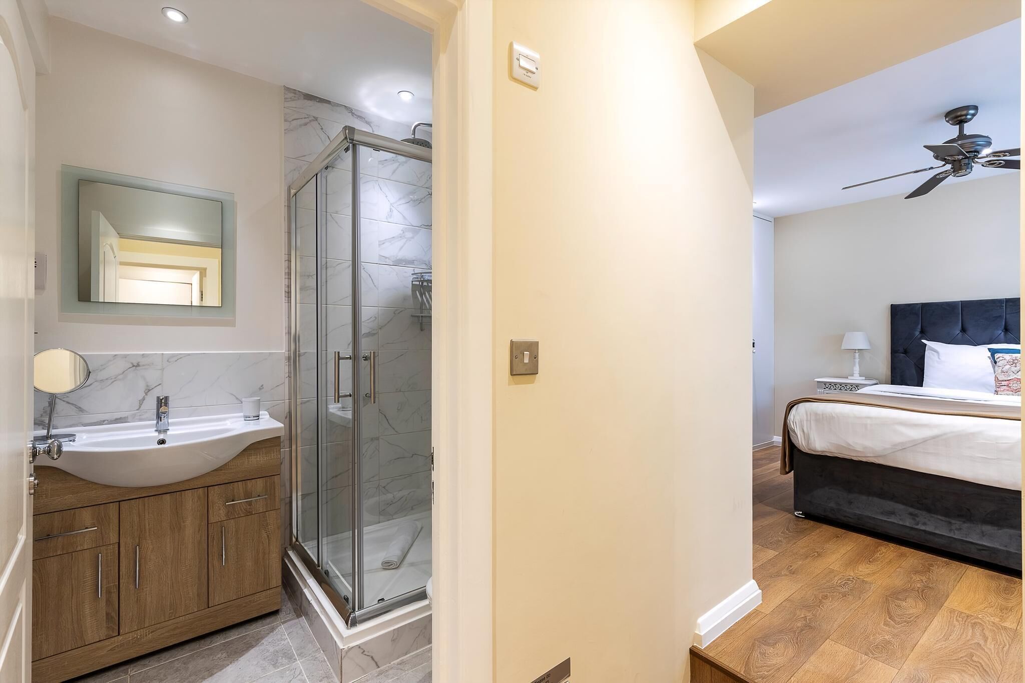 Un baño moderno con ducha de vidrio, lavamanos con encimera de mármol y muebles de madera.