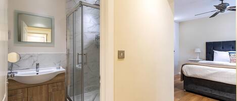 Un baño moderno con ducha de vidrio, lavamanos con encimera de mármol y muebles de madera.