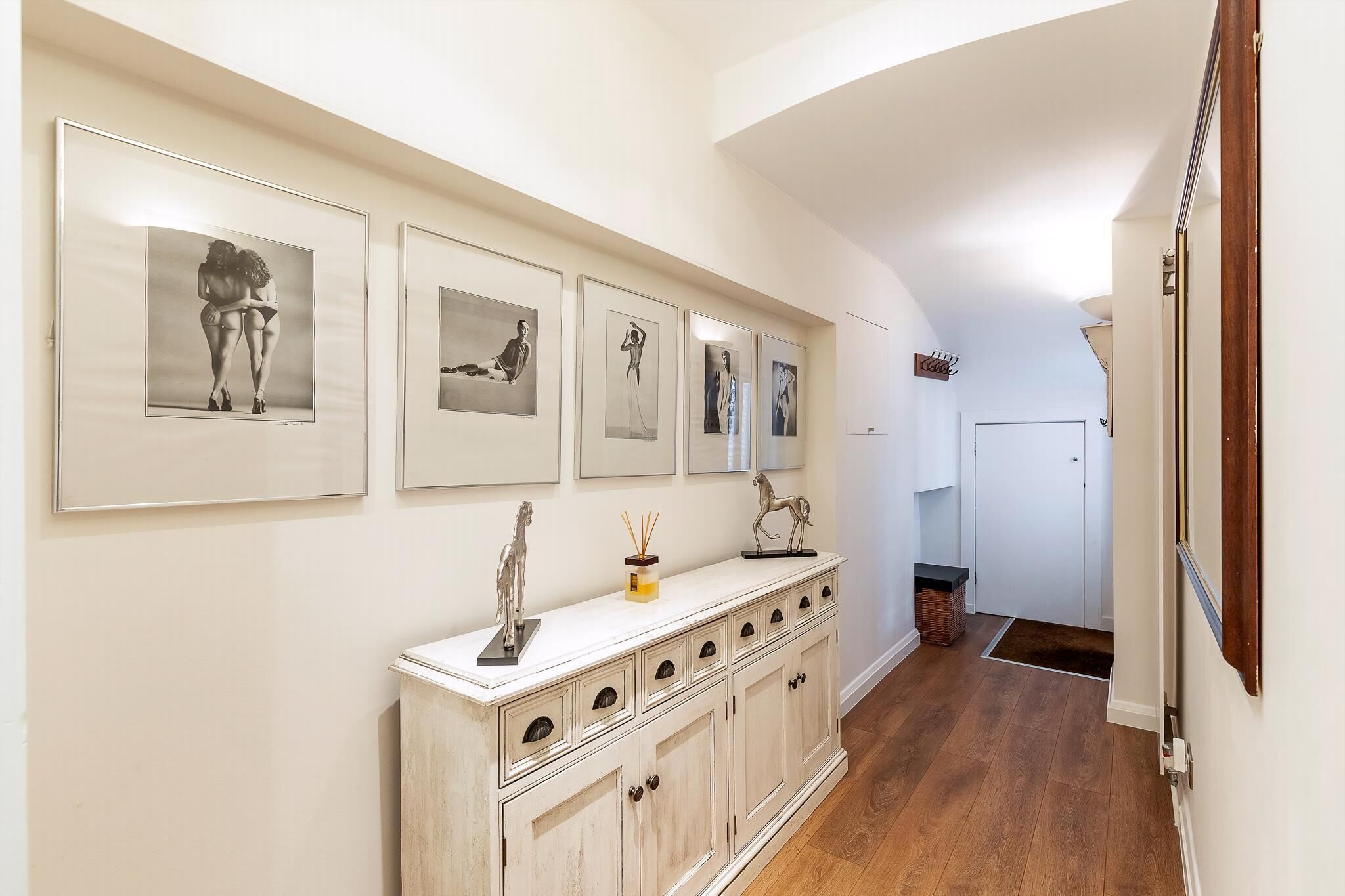 A hallway with a white cabinet, framed artwork, and a white door at the end.