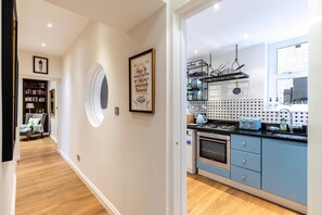 A modern kitchen with blue cabinets, a gas stove, and a microwave. There is a bookshelf and a framed quote on the wall. - Elegant Two Bedroom Flat in Redcliffe Gardens (London)