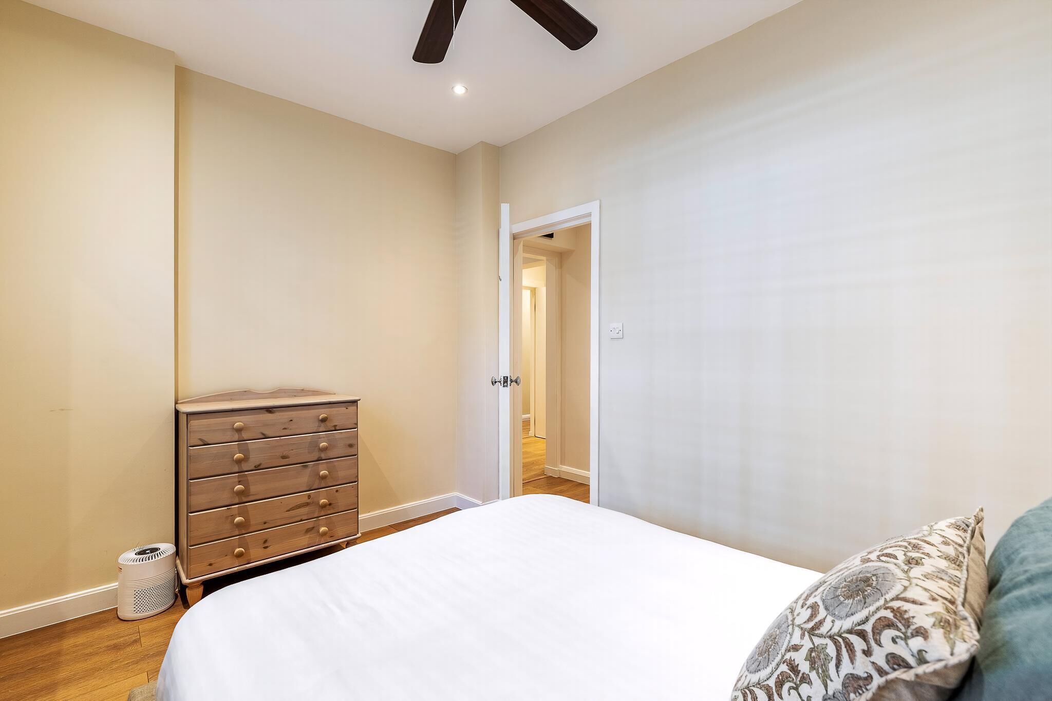 A bedroom with a bed, dresser, and a door leading to another room.