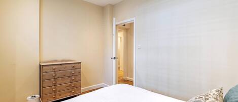 A bedroom with a bed, dresser, and a door leading to another room.