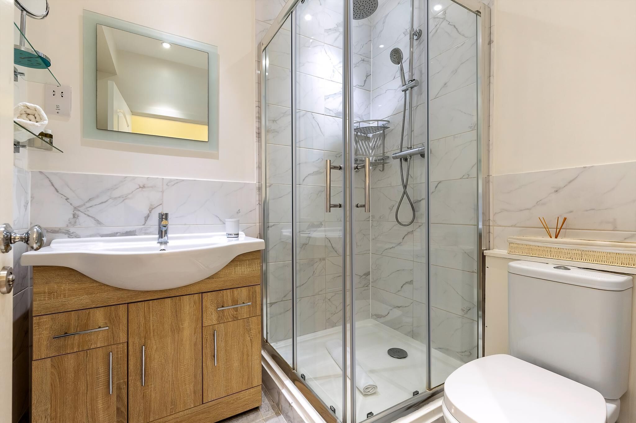 Une salle de bain moderne avec un lavabo en marbre, un meuble-lavabo en bois, une douche en verre et des toilettes.