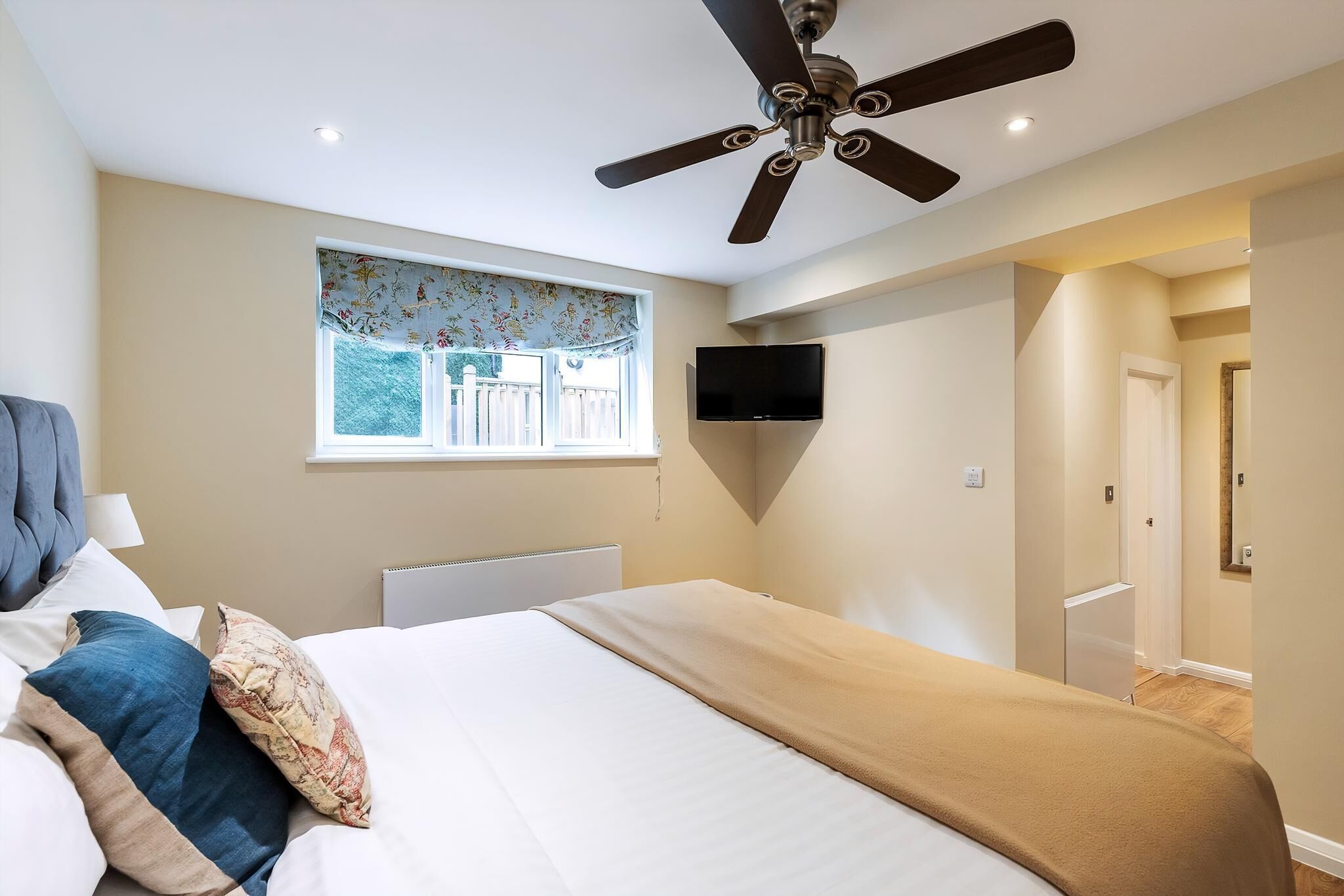 A bedroom with a bed, a ceiling fan, a window with a view, and a mounted TV.