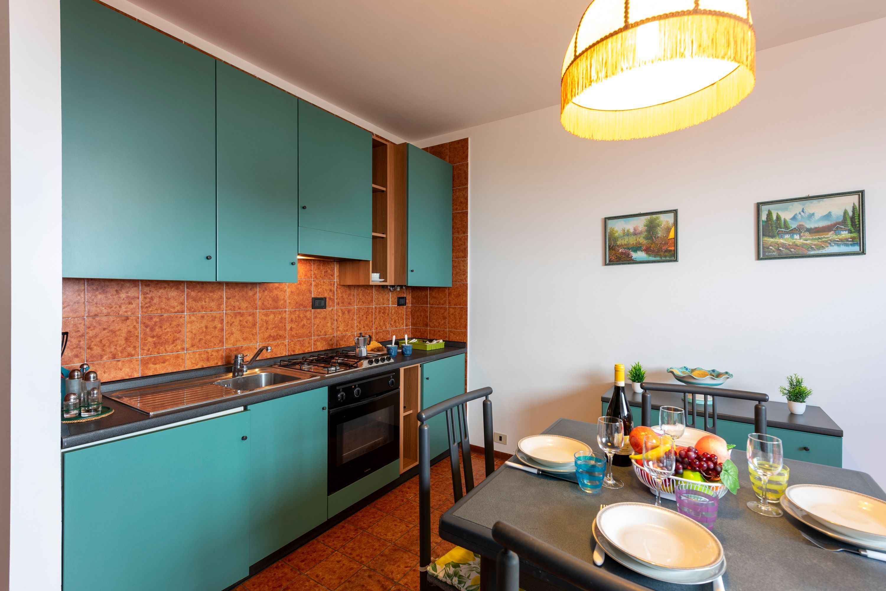 Une cuisine moderne avec des armoires de couleur turquoise, une cuisinière à gaz et un coin repas avec une table dressée pour quatre personnes.